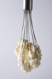 Photo of Whisk with whipped cream on white background, closeup