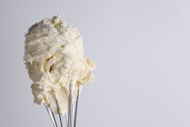 Photo of Whisk with whipped cream on white background, closeup. Space for text