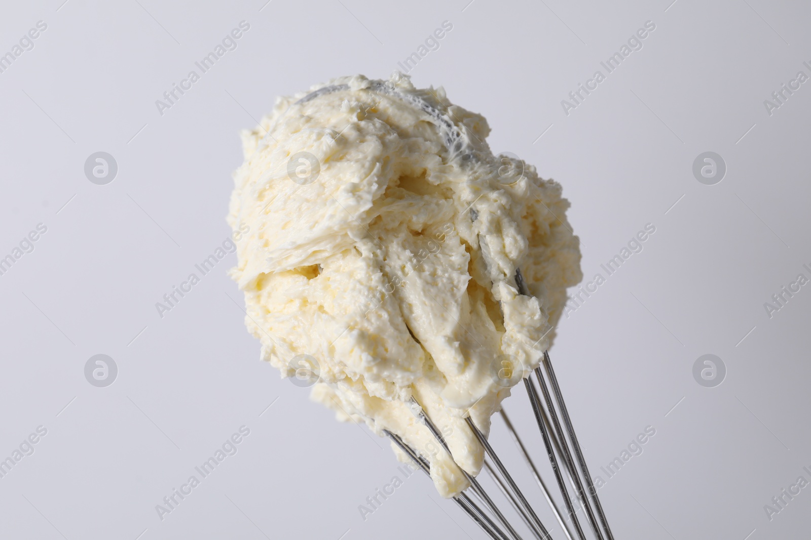 Photo of Whisk with whipped cream on white background, closeup