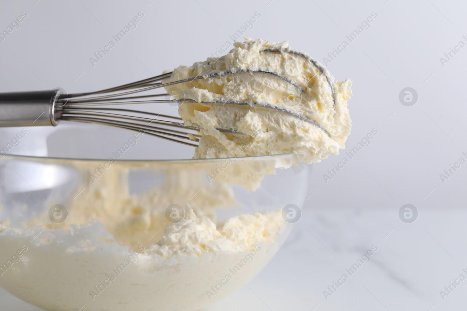 Photo of Whisk and bowl with whipped cream on white table, closeup