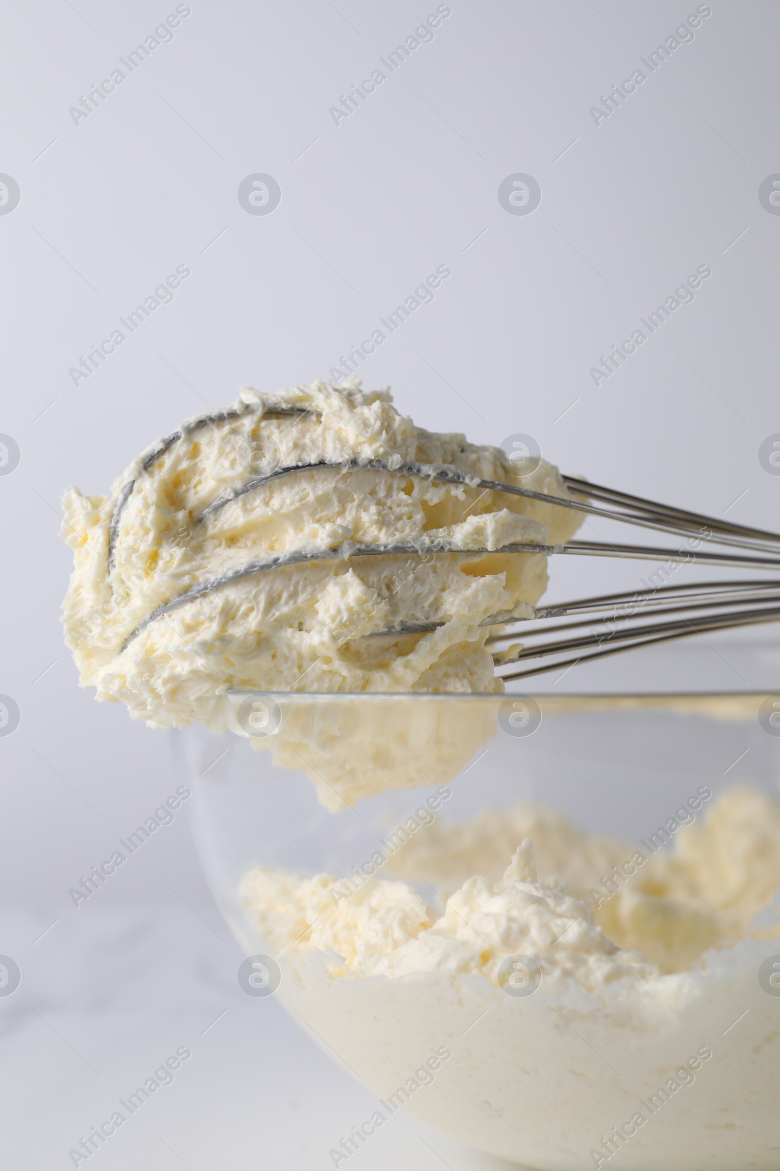 Photo of Whisk and bowl with whipped cream on white background, closeup