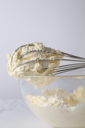 Photo of Whisk and bowl with whipped cream on white background, closeup