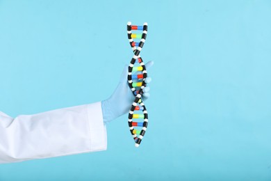 Photo of Scientist holding DNA structure model on light blue background, closeup. Space for text