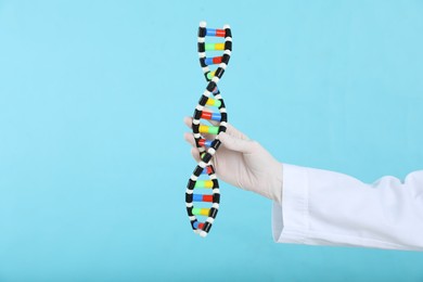 Photo of Scientist holding DNA structure model on light blue background, closeup