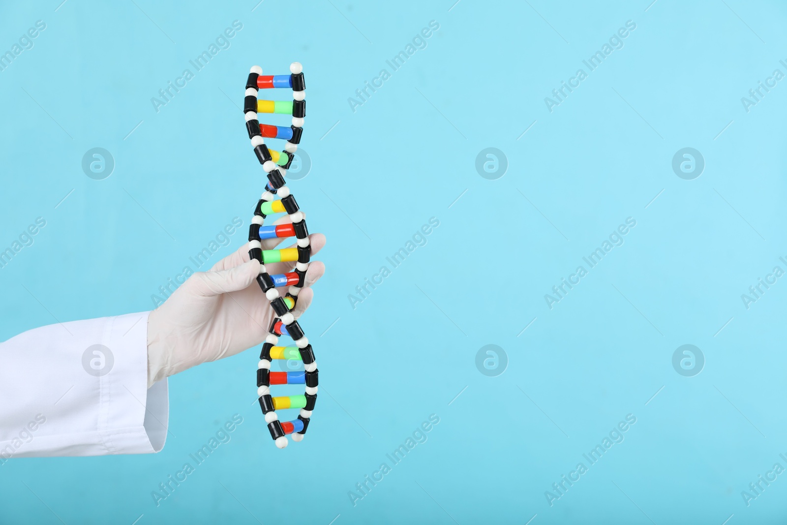 Photo of Scientist holding DNA structure model on light blue background, closeup. Space for text