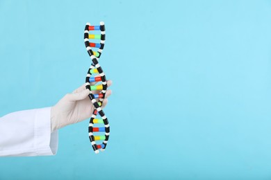 Photo of Scientist holding DNA structure model on light blue background, closeup. Space for text