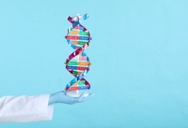 Photo of Scientist holding DNA structure model on light blue background, closeup. Space for text