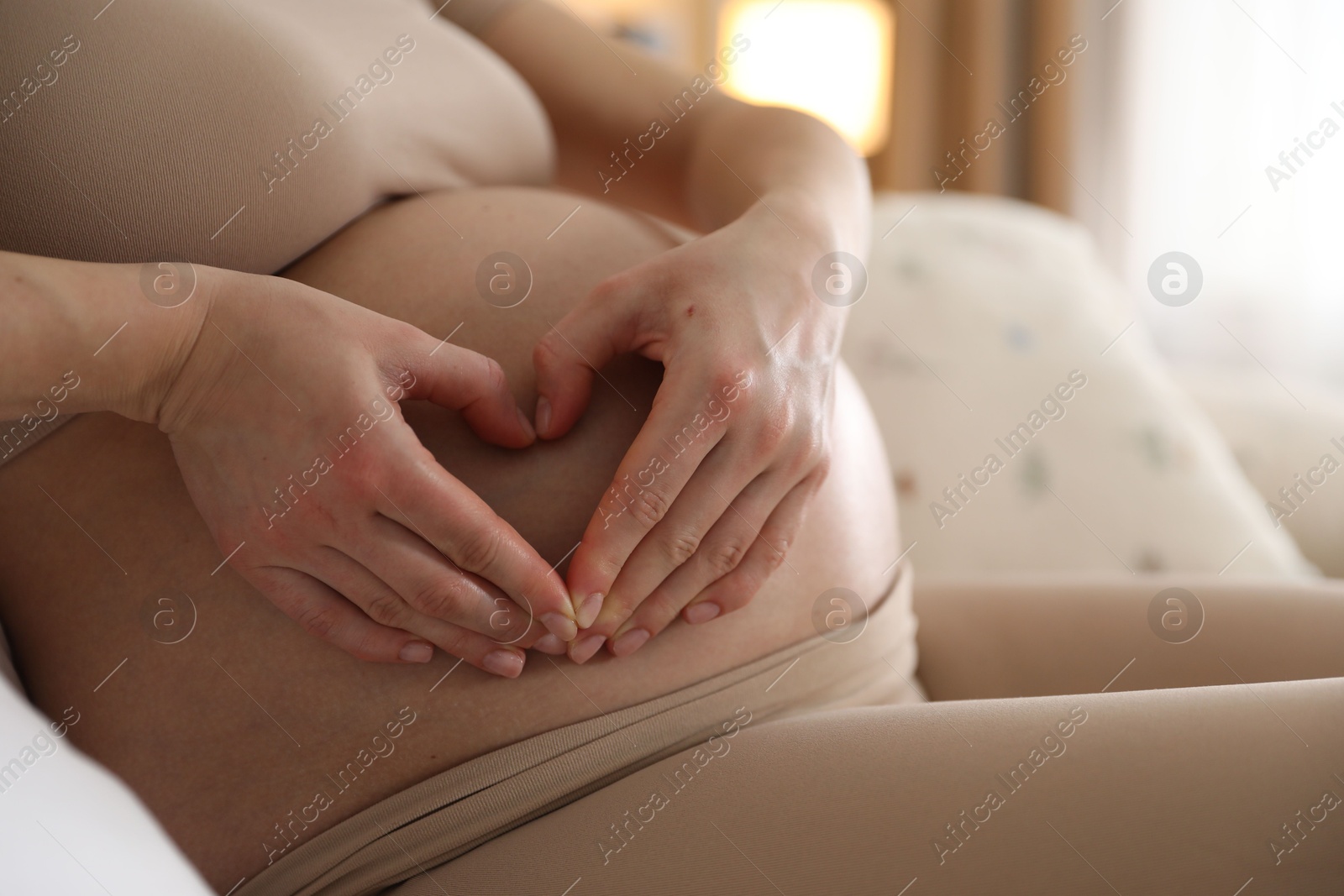 Photo of Pregnant woman making heart with hands on her belly at home, closeup