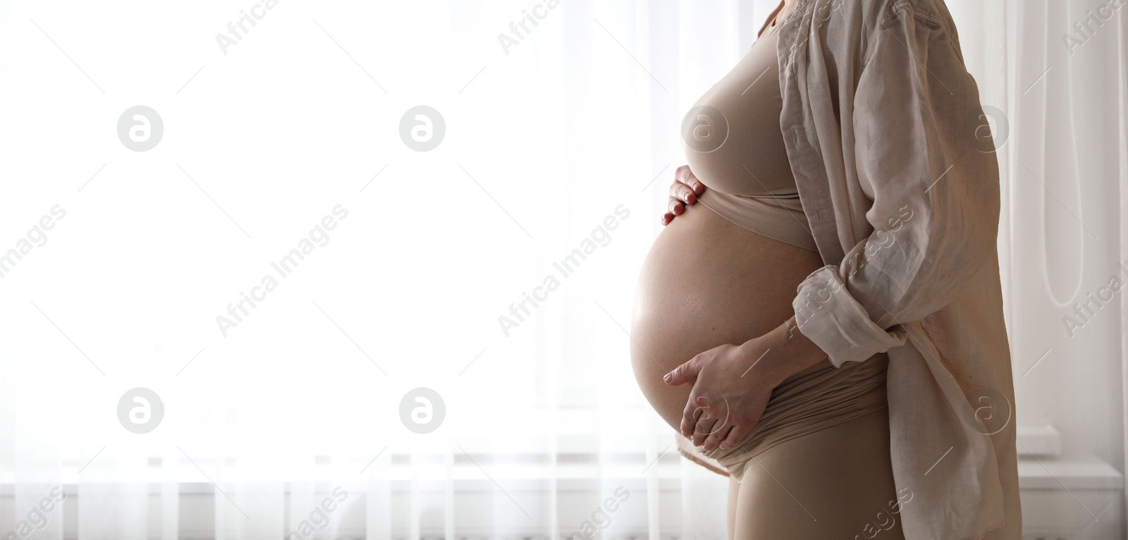 Photo of Pregnant woman near window at home, closeup. Space for text