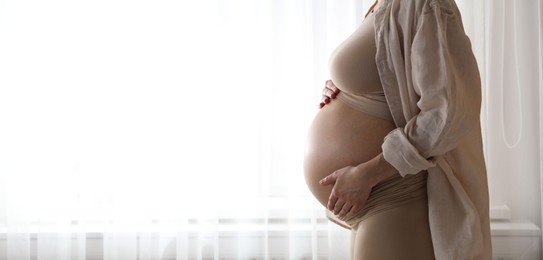 Pregnant woman near window at home, closeup. Space for text