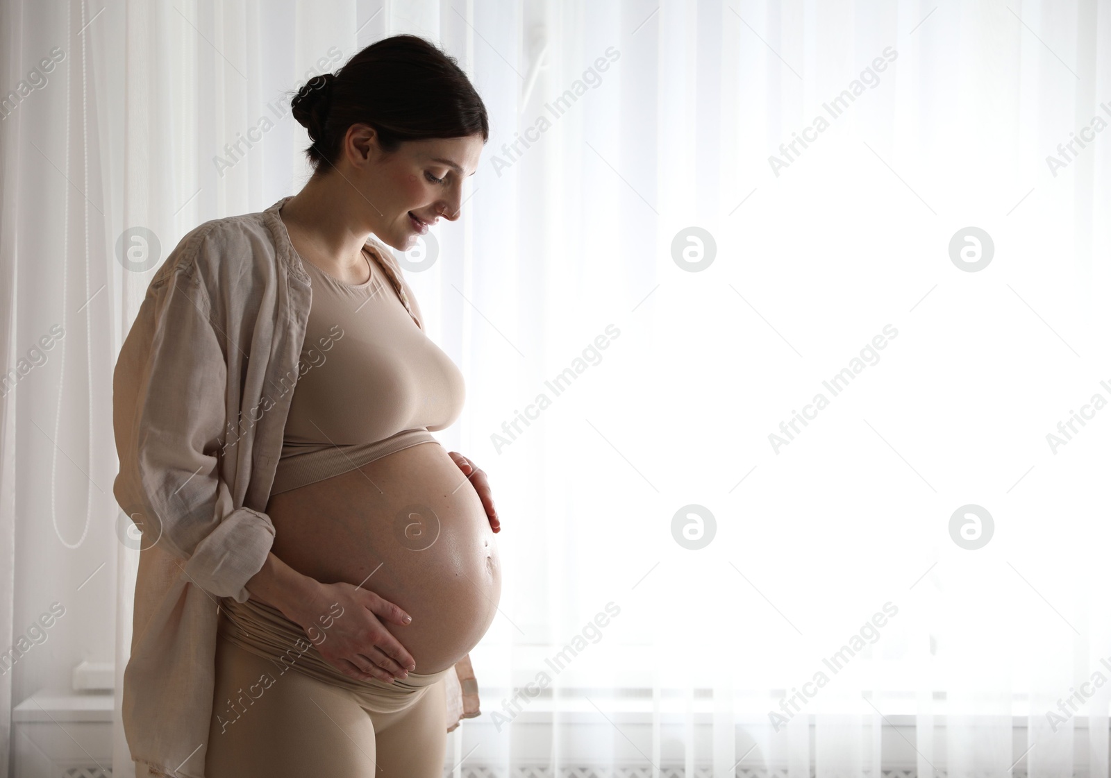 Photo of Beautiful pregnant woman near window at home. Space for text