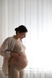 Beautiful pregnant woman near window at home