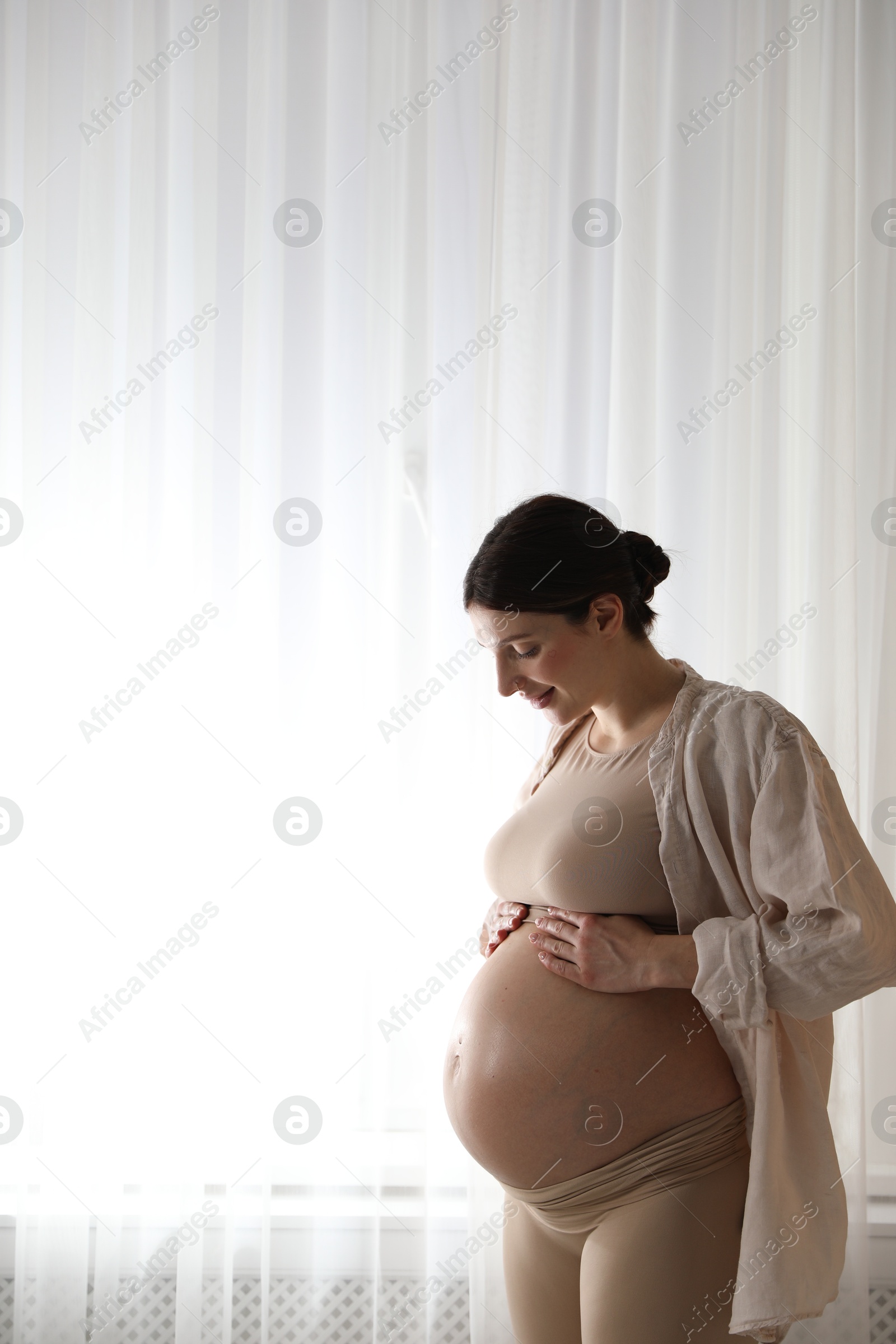 Photo of Beautiful pregnant woman near window at home