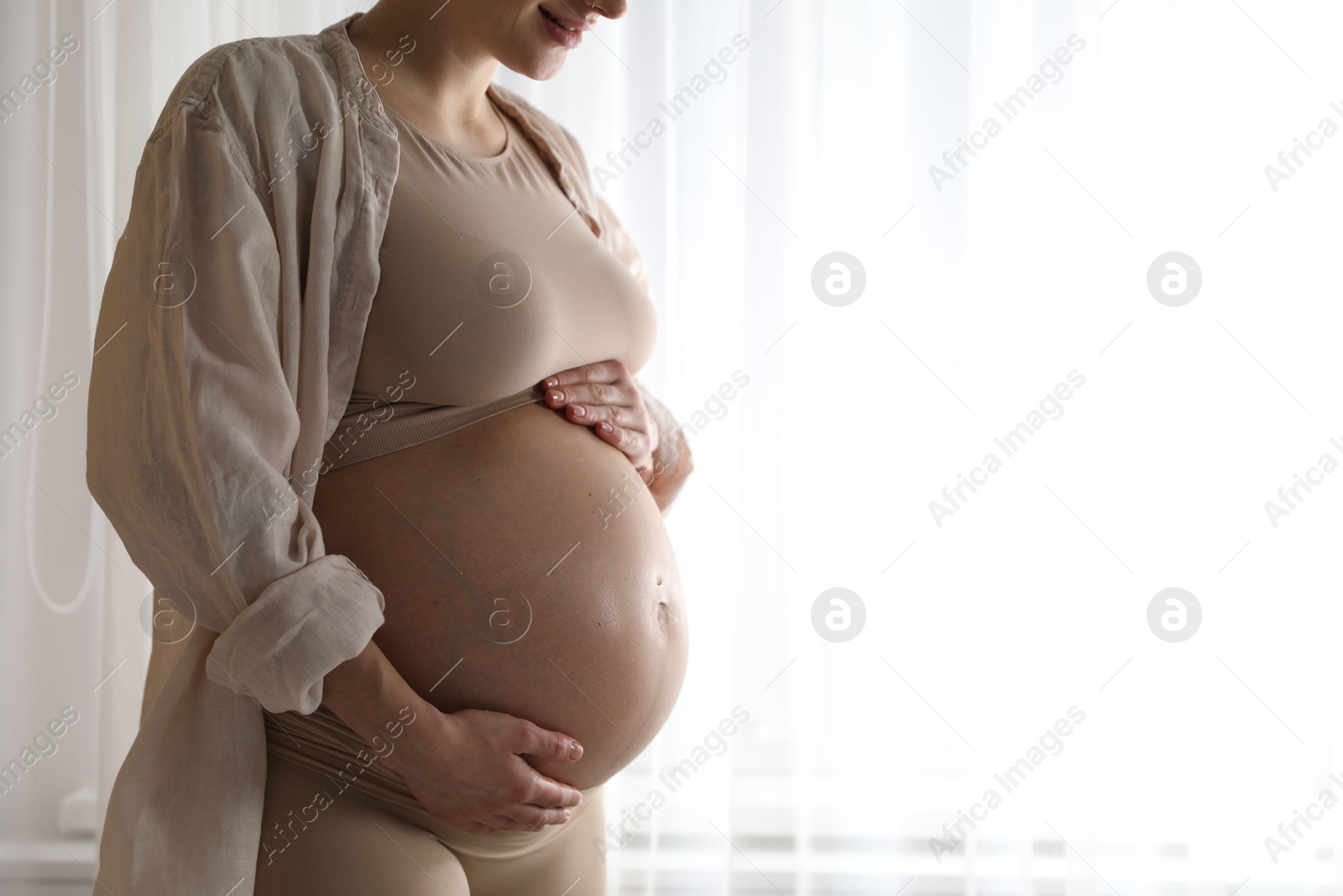 Photo of Pregnant woman near window at home, closeup. Space for text