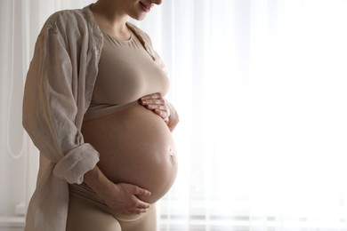 Photo of Pregnant woman near window at home, closeup. Space for text