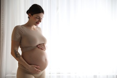 Photo of Beautiful pregnant woman near window at home. Space for text