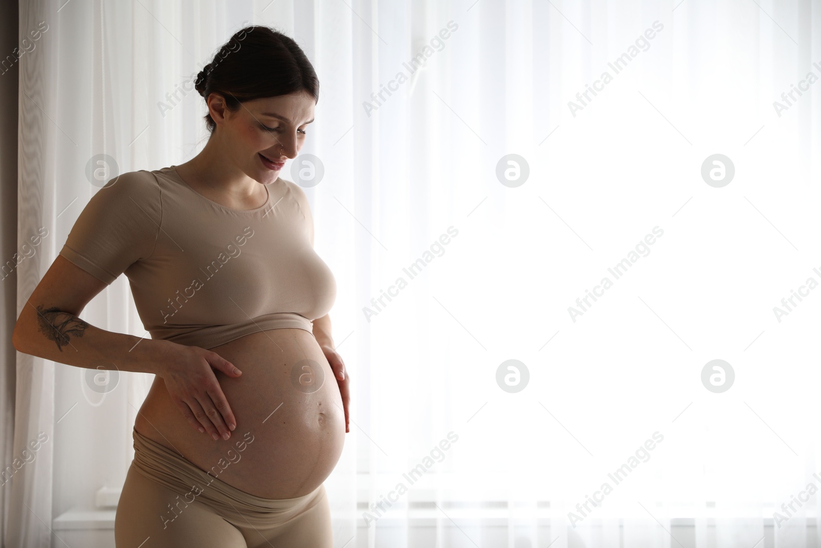 Photo of Beautiful pregnant woman near window at home. Space for text