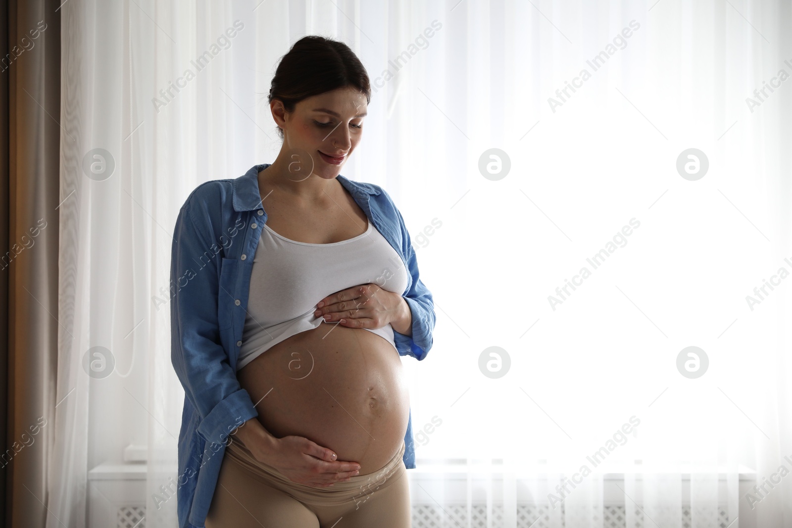 Photo of Beautiful pregnant woman near window at home. Space for text