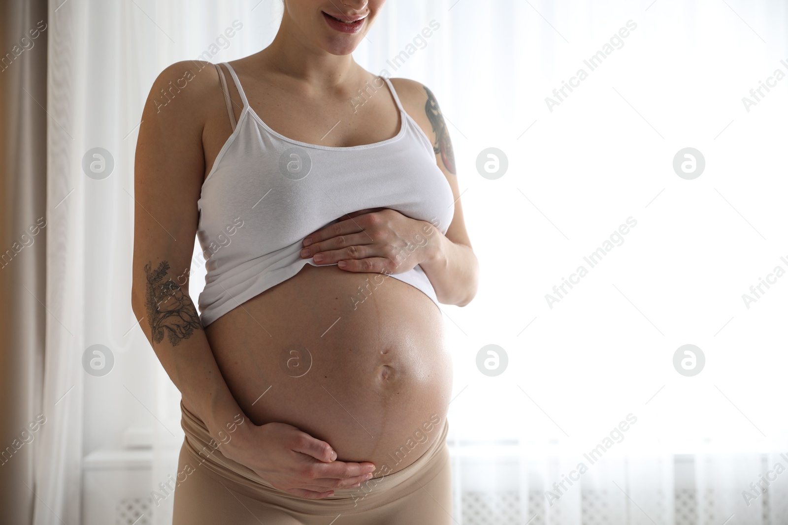 Photo of Pregnant woman near window at home, closeup. Space for text