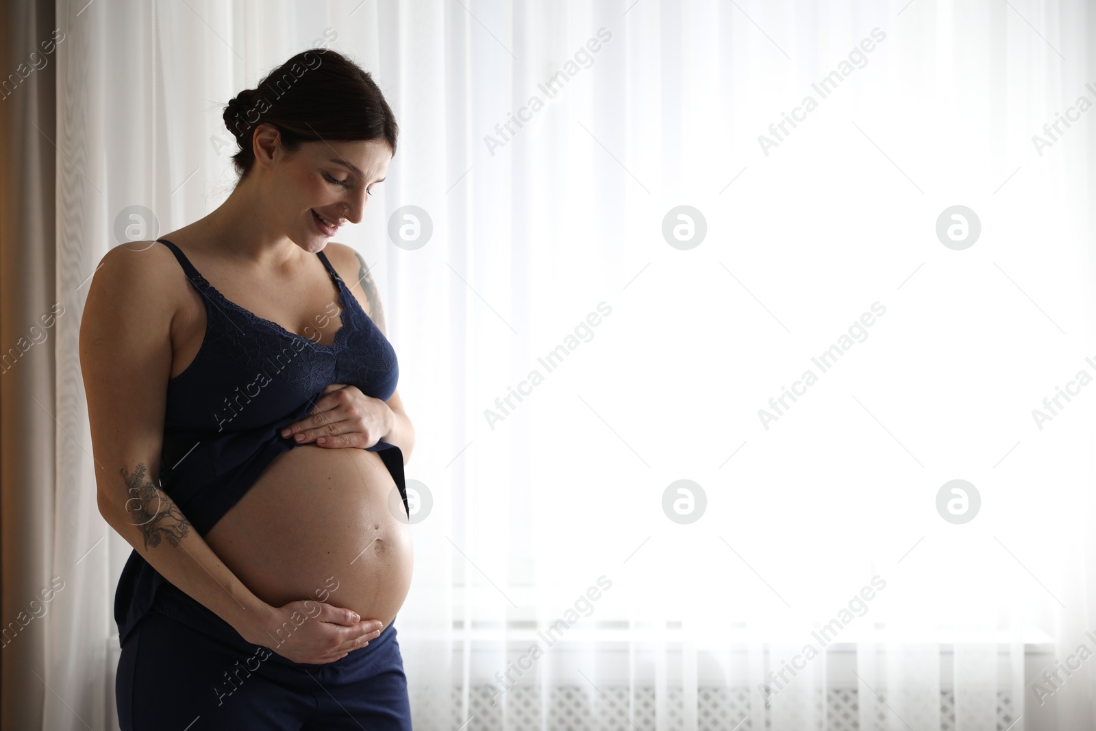 Photo of Beautiful pregnant woman near window at home. Space for text