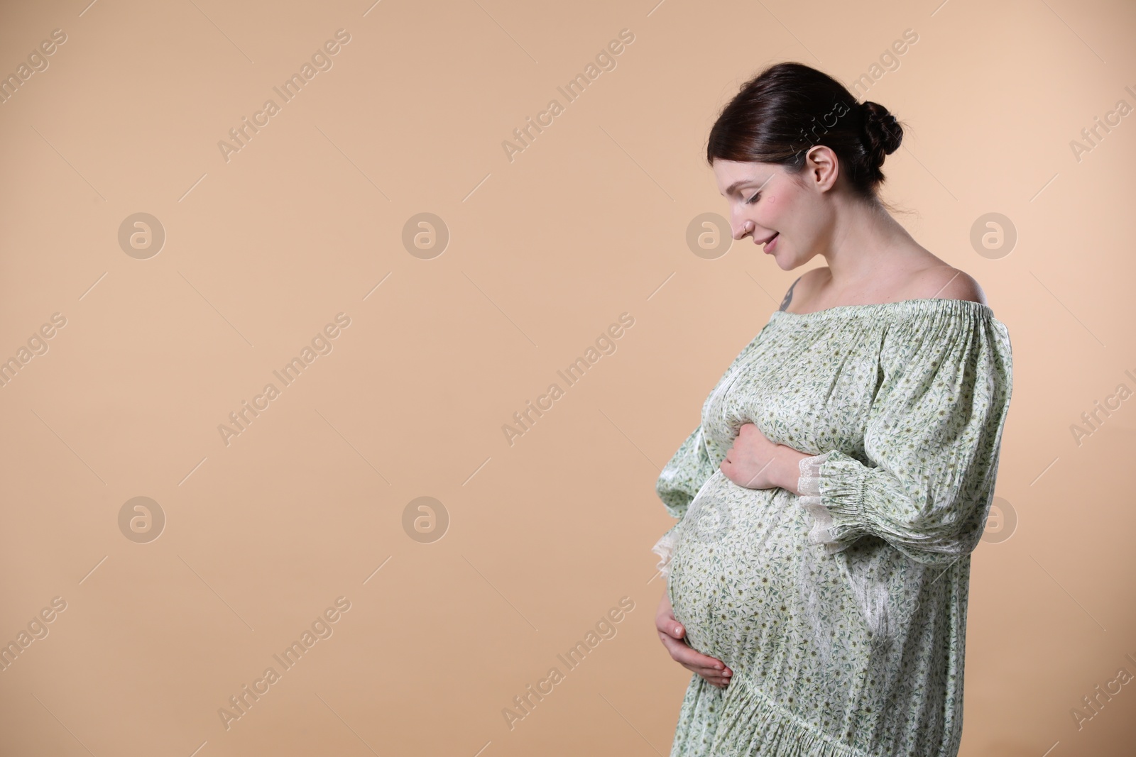 Photo of Beautiful pregnant woman with cute belly on beige background. Space for text