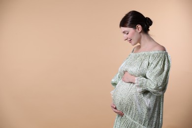 Photo of Beautiful pregnant woman with cute belly on beige background. Space for text