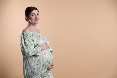 Photo of Beautiful pregnant woman with cute belly on beige background. Space for text