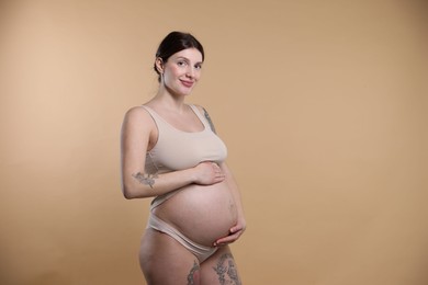 Photo of Beautiful pregnant woman with cute belly on beige background. Space for text