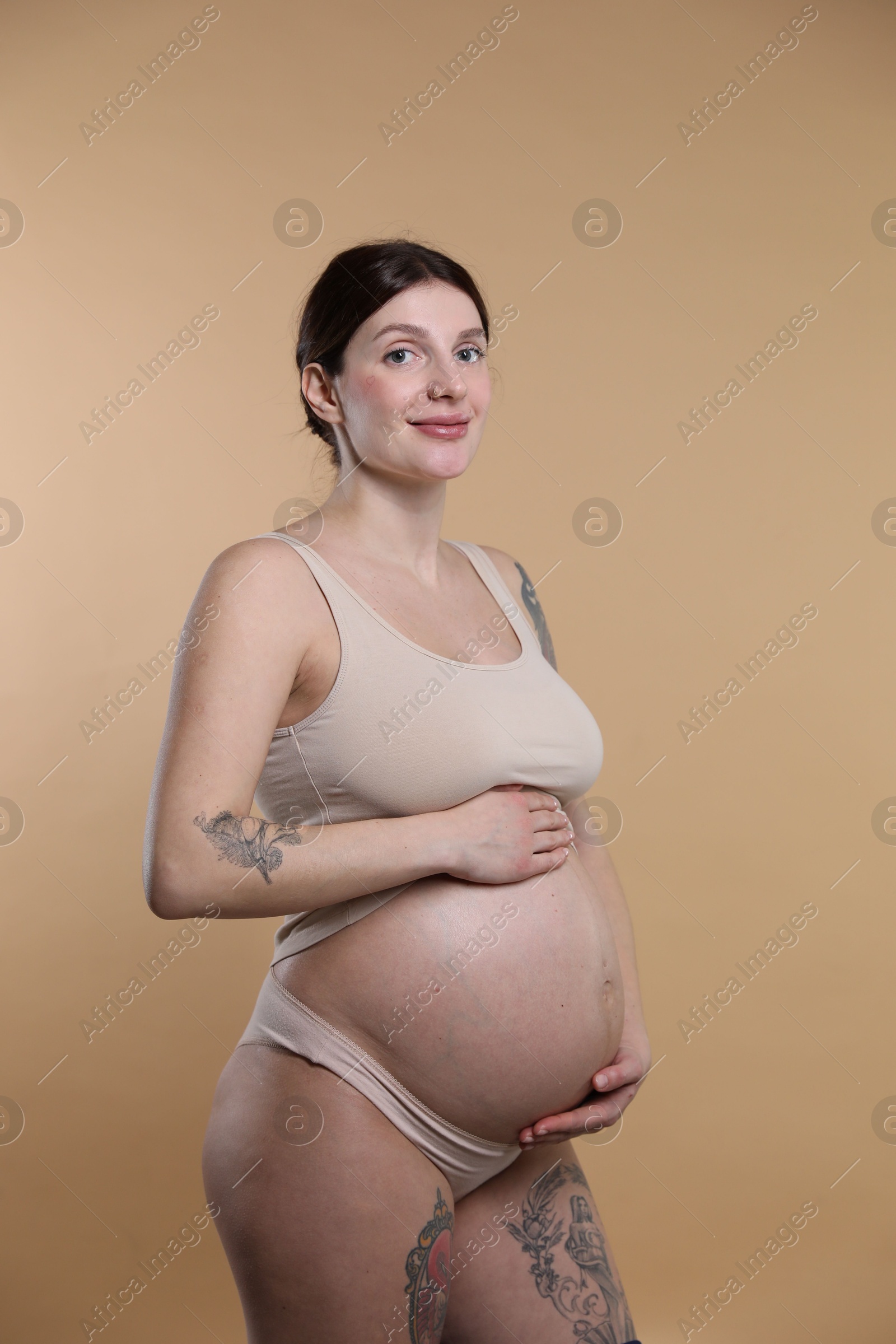 Photo of Beautiful pregnant woman with cute belly on beige background