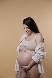 Photo of Beautiful pregnant woman with cute belly on beige background