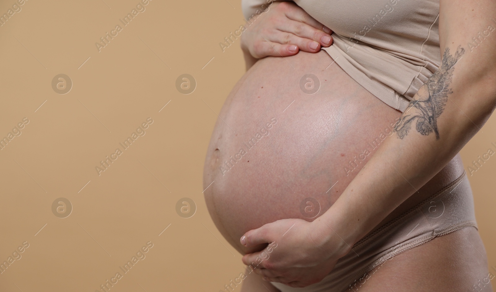 Photo of Pregnant woman with cute belly on beige background, closeup. Space for text