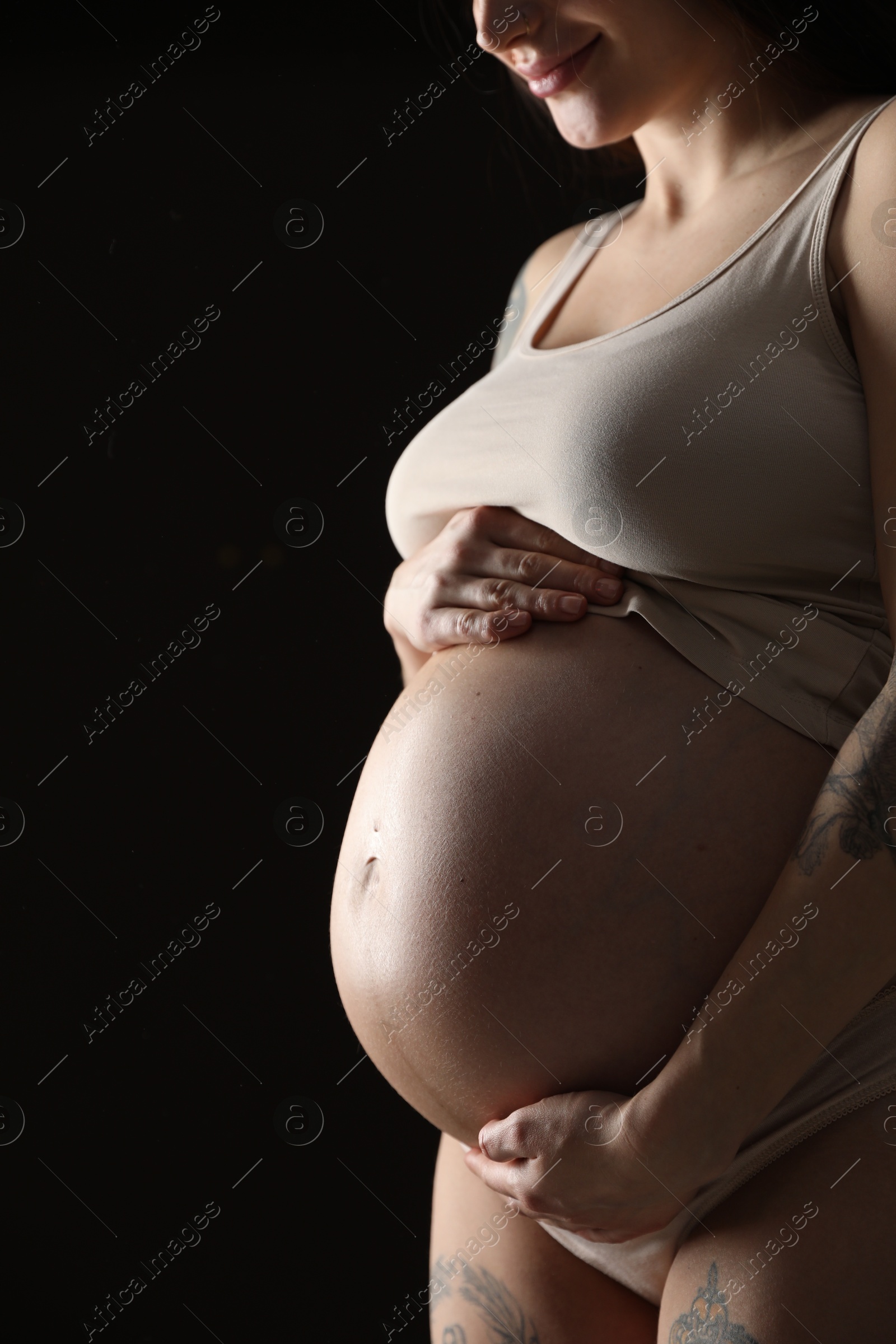 Photo of Pregnant woman with cute belly on black background, closeup