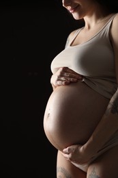 Pregnant woman with cute belly on black background, closeup