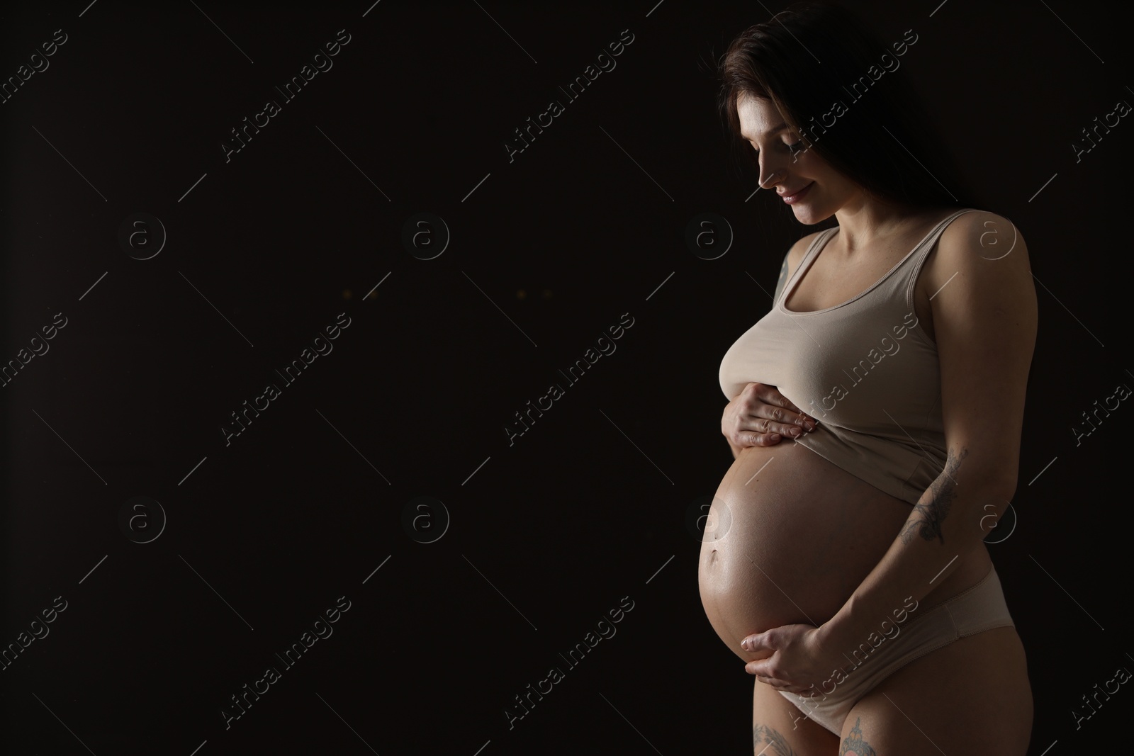 Photo of Beautiful pregnant woman with cute belly on black background. Space for text