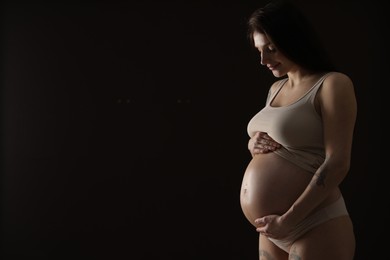 Photo of Beautiful pregnant woman with cute belly on black background. Space for text