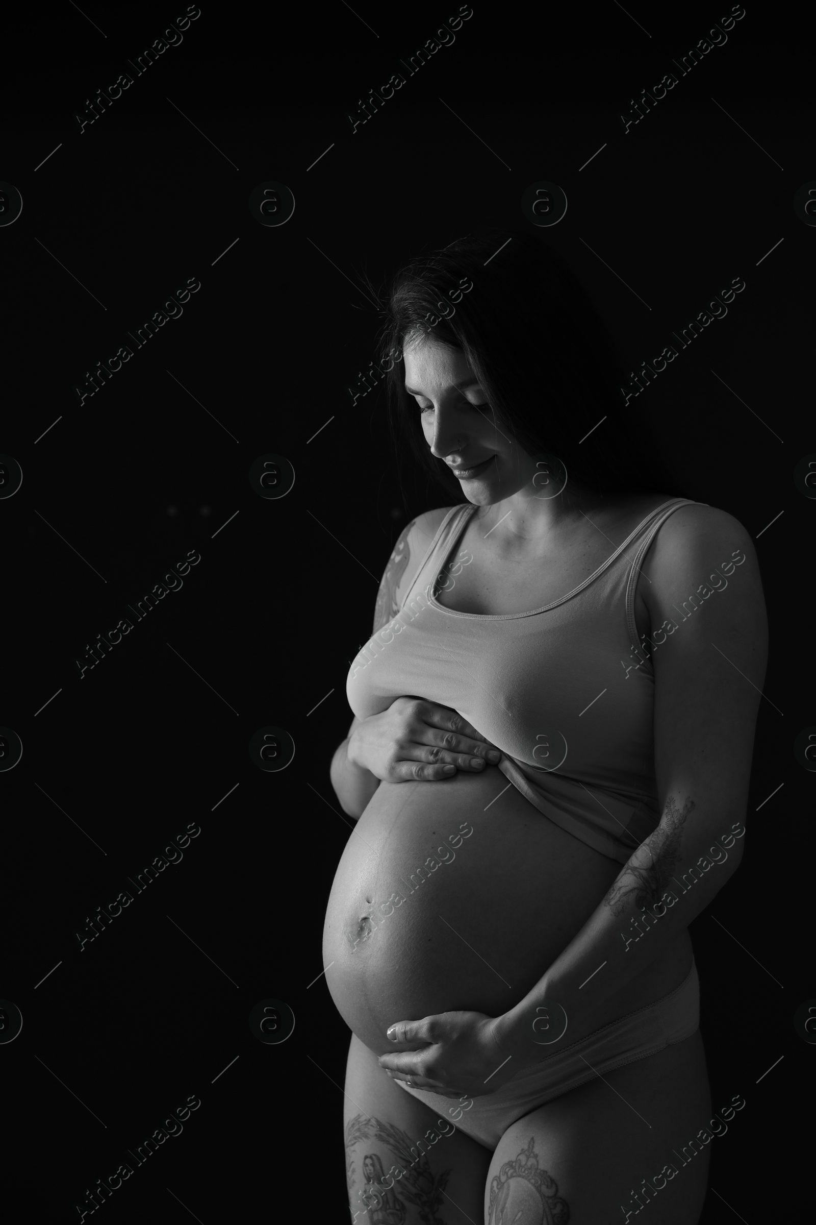 Photo of Beautiful pregnant woman with cute belly on dark background. Black and white effect