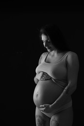 Photo of Beautiful pregnant woman with cute belly on dark background. Black and white effect