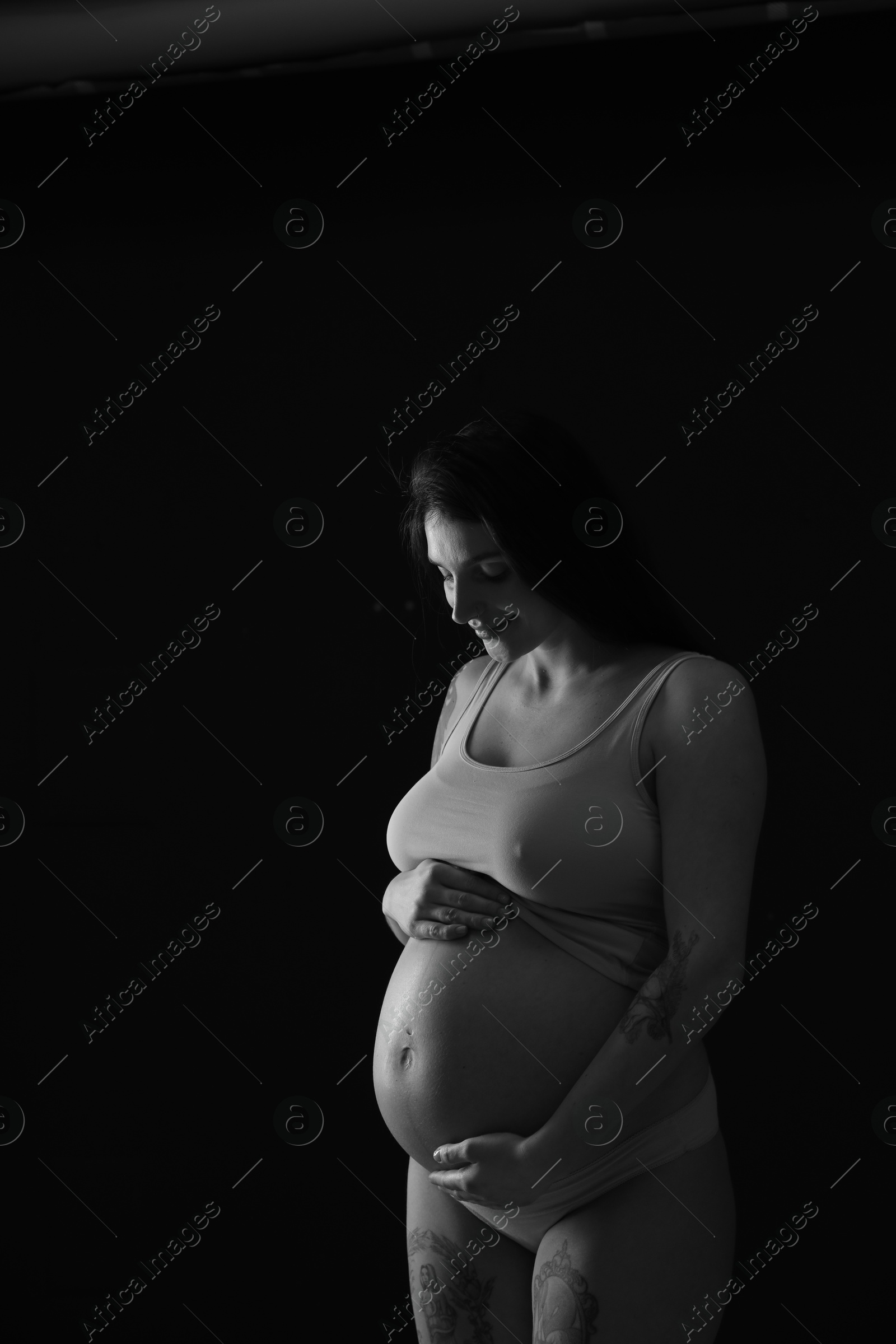 Photo of Beautiful pregnant woman with cute belly on dark background. Black and white effect