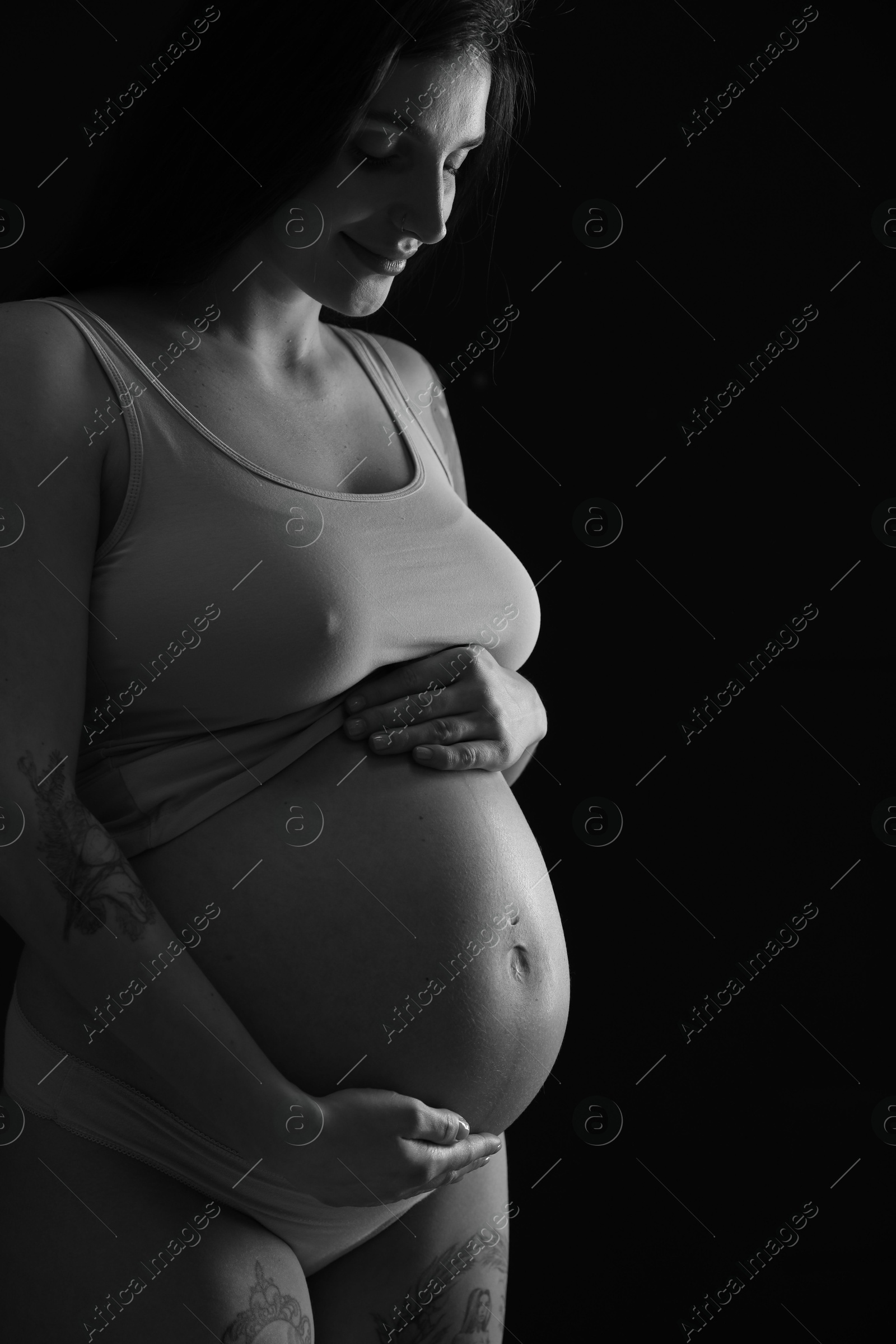 Photo of Beautiful pregnant woman with cute belly on dark background. Black and white effect