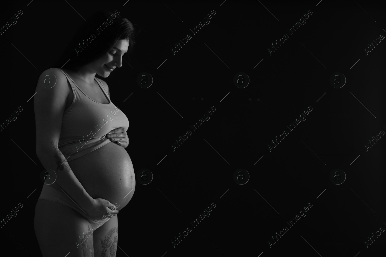 Photo of Beautiful pregnant woman with cute belly on dark background, space for text. Black and white effect