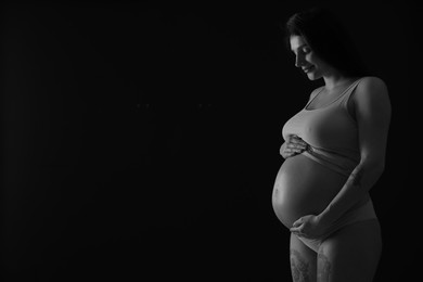 Photo of Beautiful pregnant woman with cute belly on dark background, space for text. Black and white effect