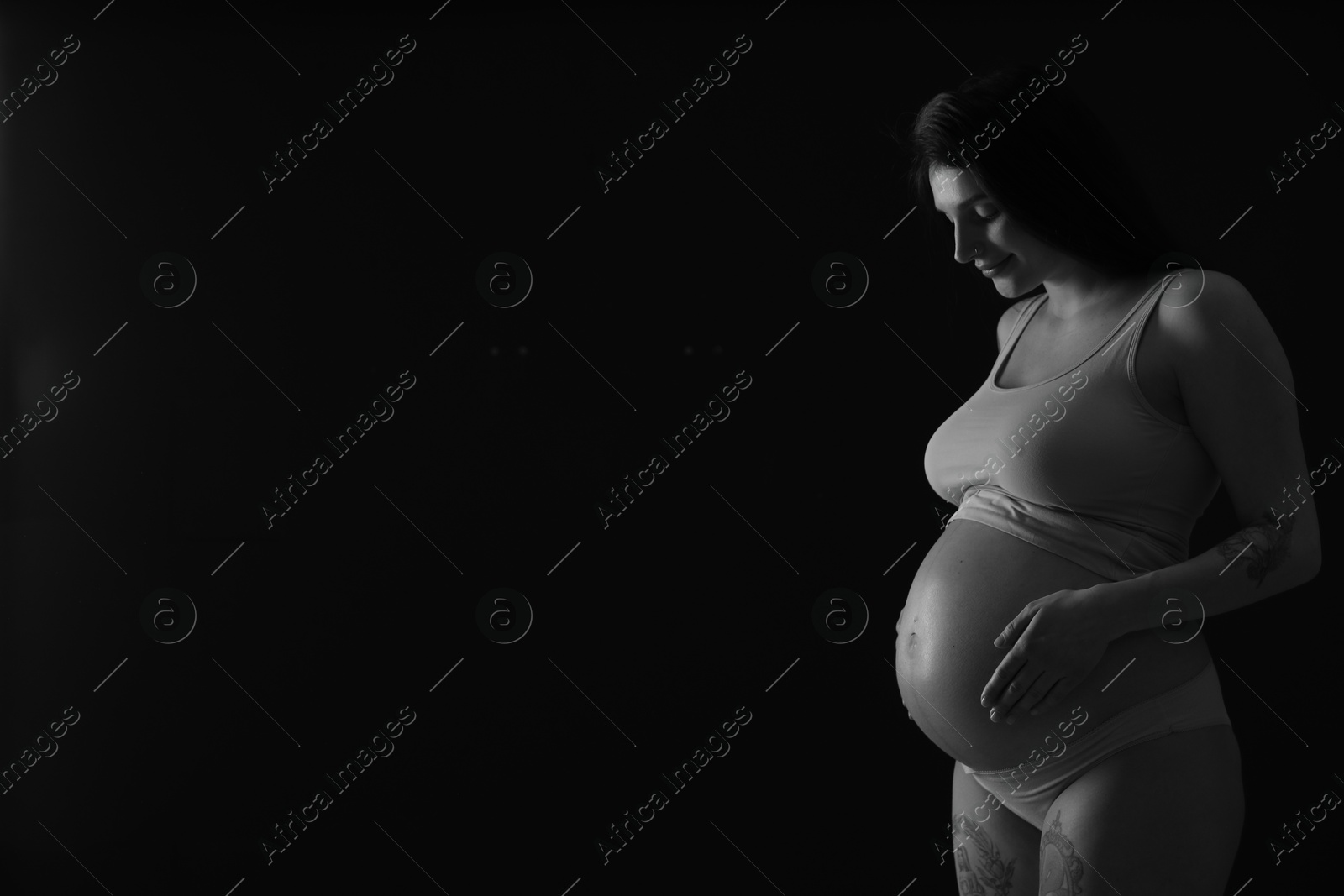 Photo of Beautiful pregnant woman with cute belly on dark background, space for text. Black and white effect