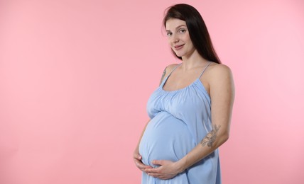 Beautiful pregnant woman with cute belly on pink background. Space for text