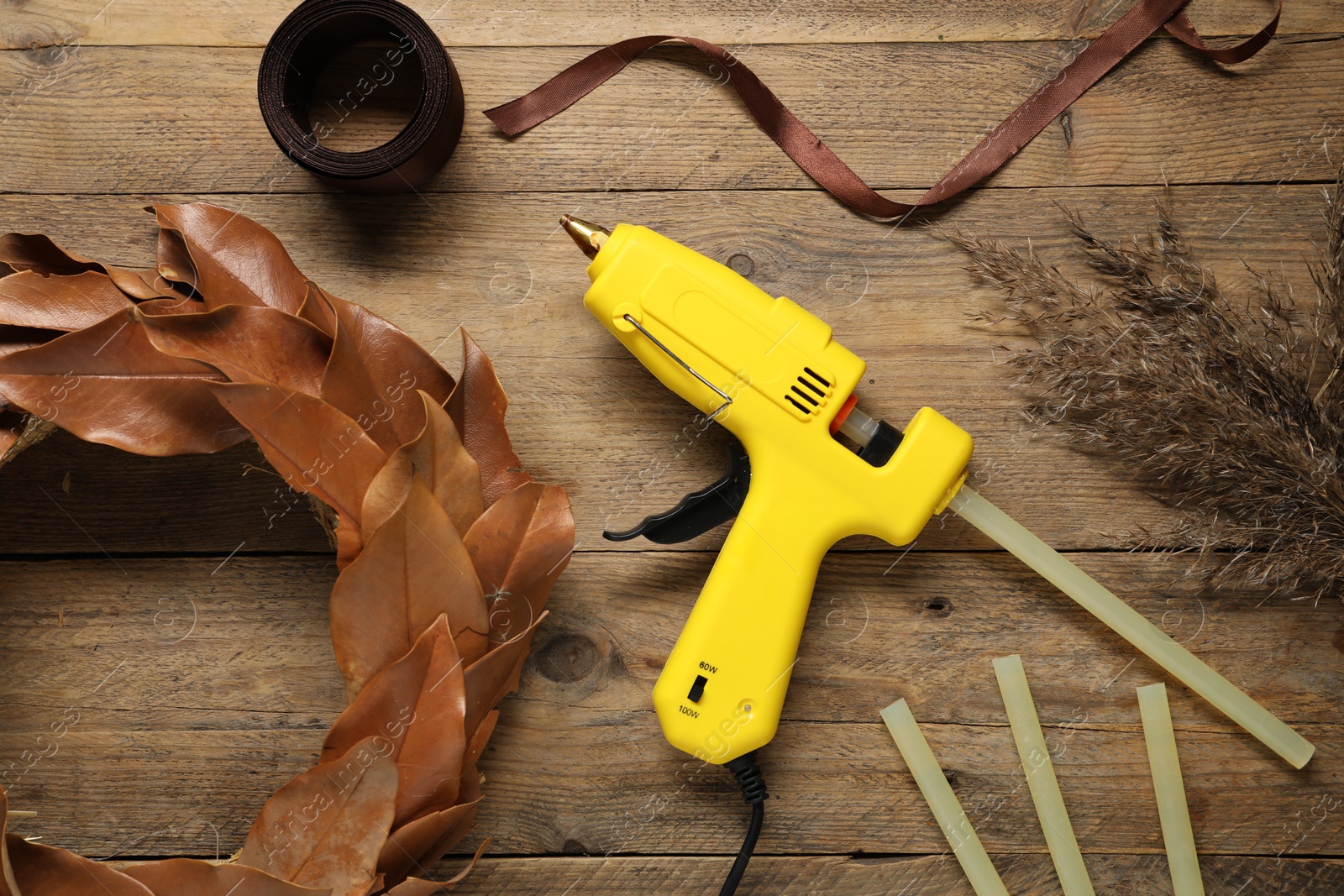 Photo of Hot glue gun and handicraft materials on wooden table, flat lay