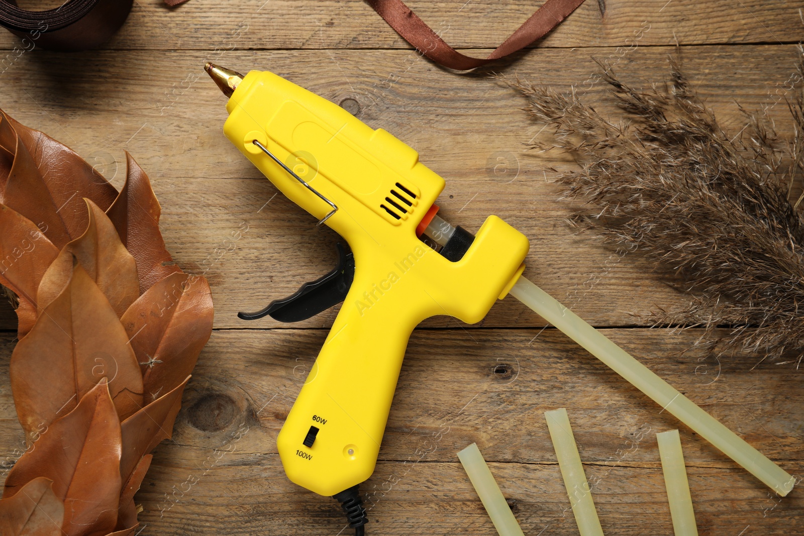 Photo of Hot glue gun and handicraft materials on wooden table, flat lay