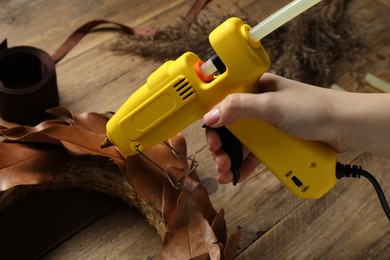 Photo of Woman with hot glue gun making craft at wooden table, closeup