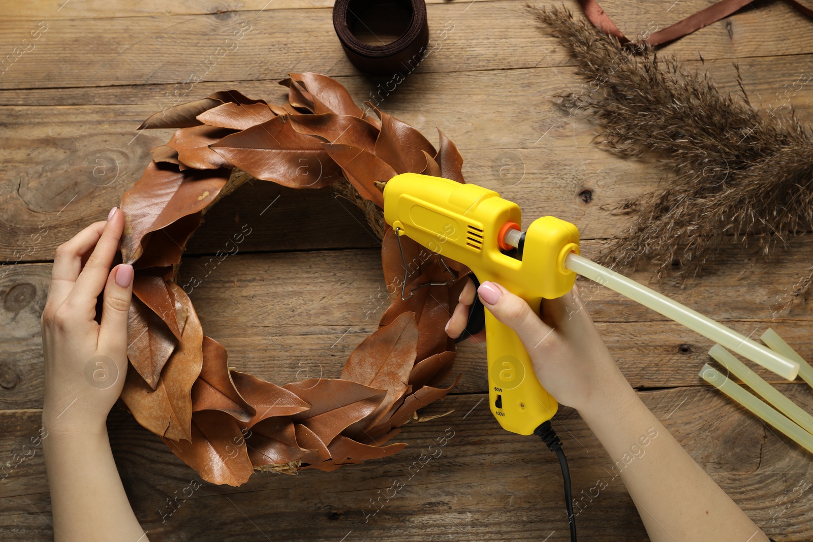 Photo of Woman with hot glue gun making craft at wooden table, top view