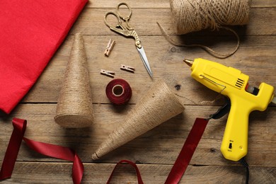 Photo of Hot glue gun and handicraft materials on wooden table, flat lay