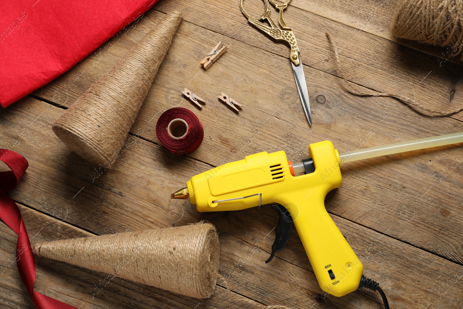 Photo of Hot glue gun and handicraft materials on wooden table, flat lay