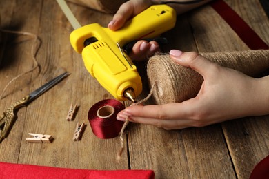 Photo of Woman with hot glue gun making craft at wooden table, closeup